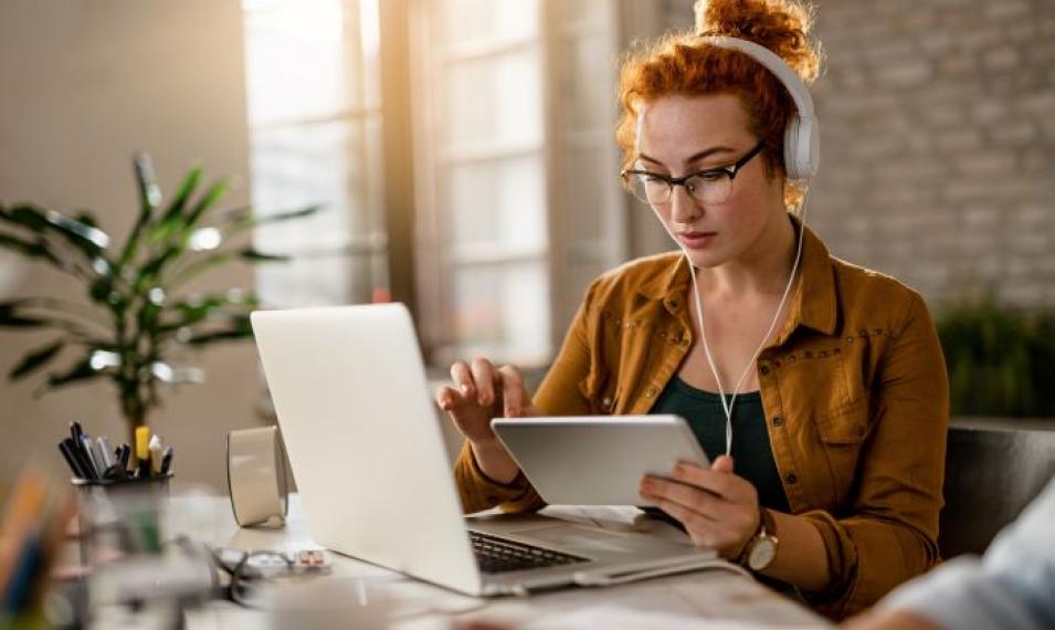 young-creative-businesswoman-working-digital-tablet-while-wearing-headphones-office