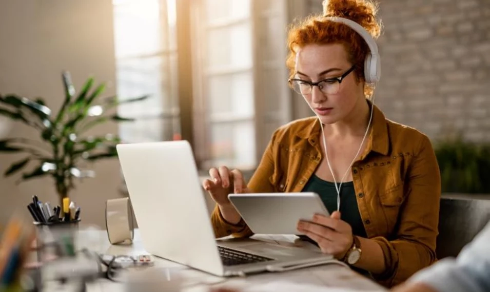 young-creative-businesswoman-working-digital-tablet-while-wearing-headphones-office